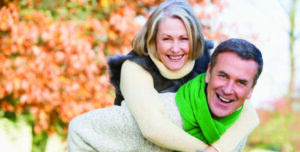 Senior man giving woman piggyback ride through autumn woods